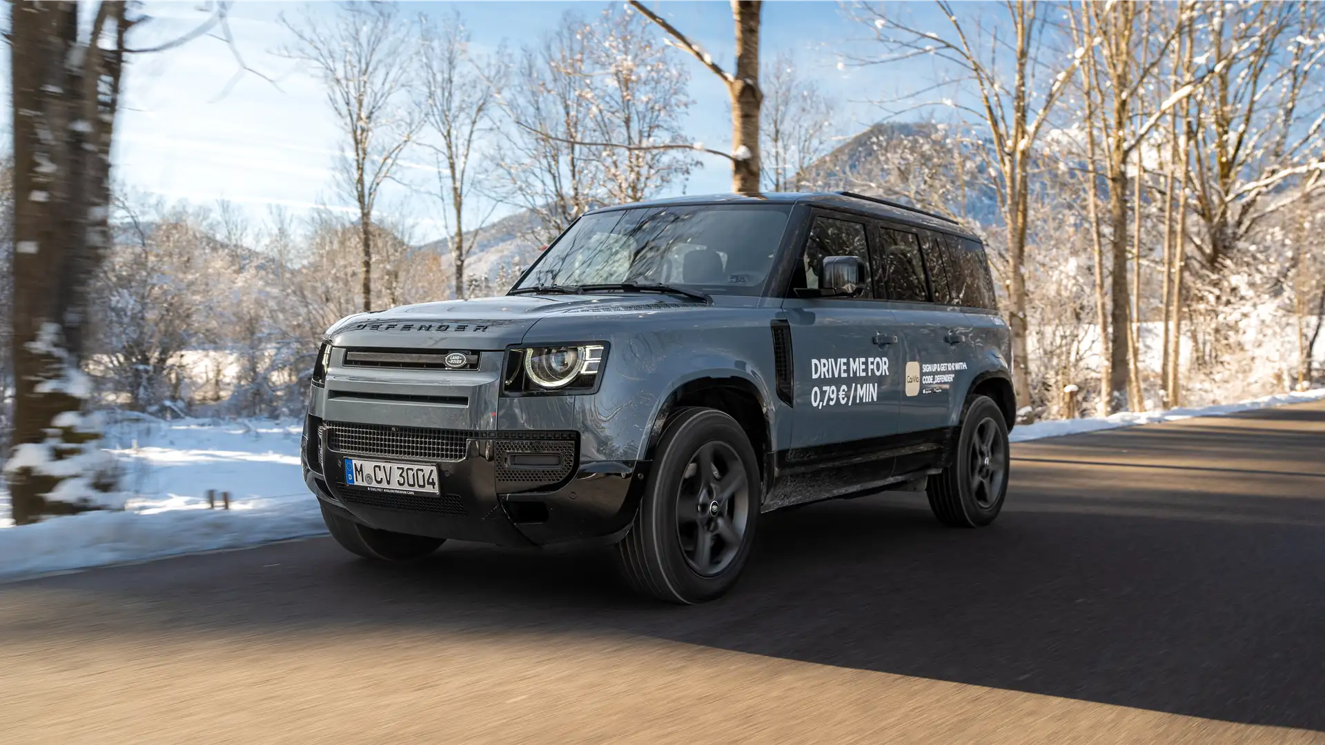 Neuer Land Rover Defender des Carsharing Angebots auf geteerten Straße in winterlicher Landschaft bei sonnigem Wetter