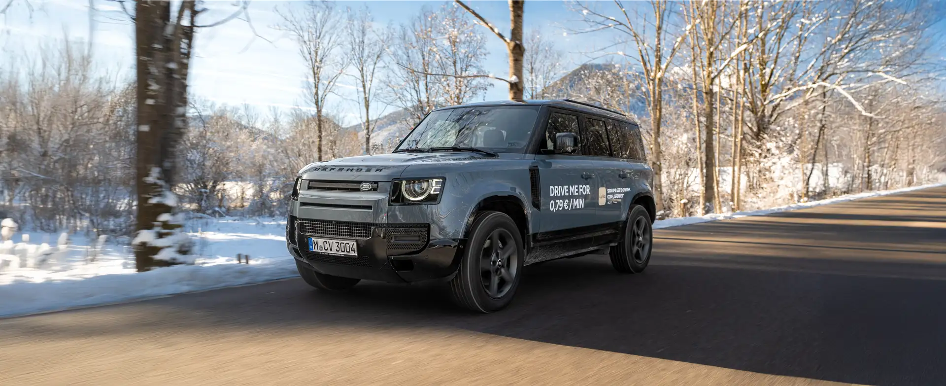Neuer Land Rover Defender des Carsharing Angebots auf geteerten Straße in winterlicher Landschaft bei sonnigem Wetter