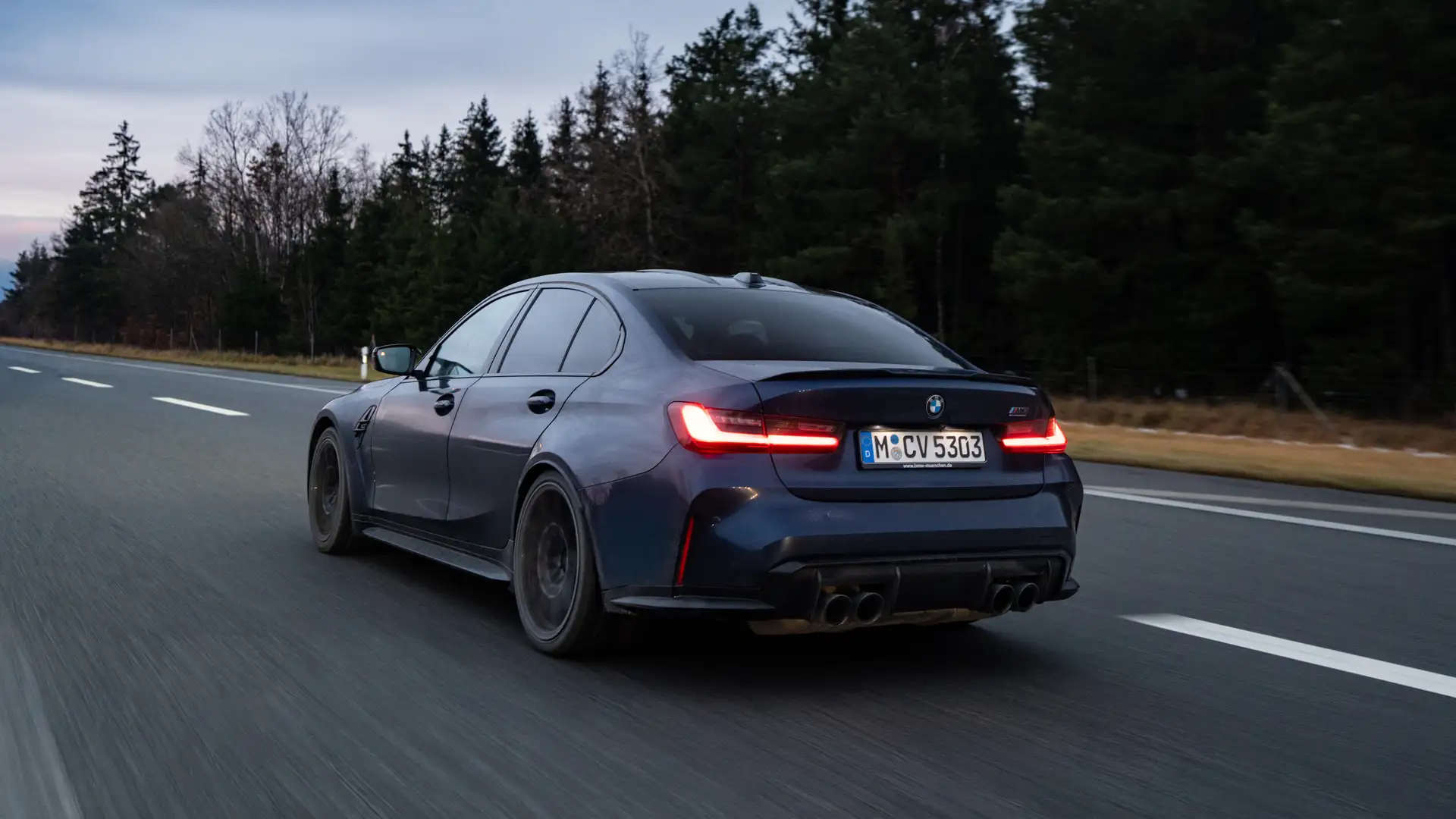 BMW M3 fährt bei Abenddämmerung auf der Autobahn zurück nach München, mit warmem Himmel und vorbeiziehender Landschaft.
