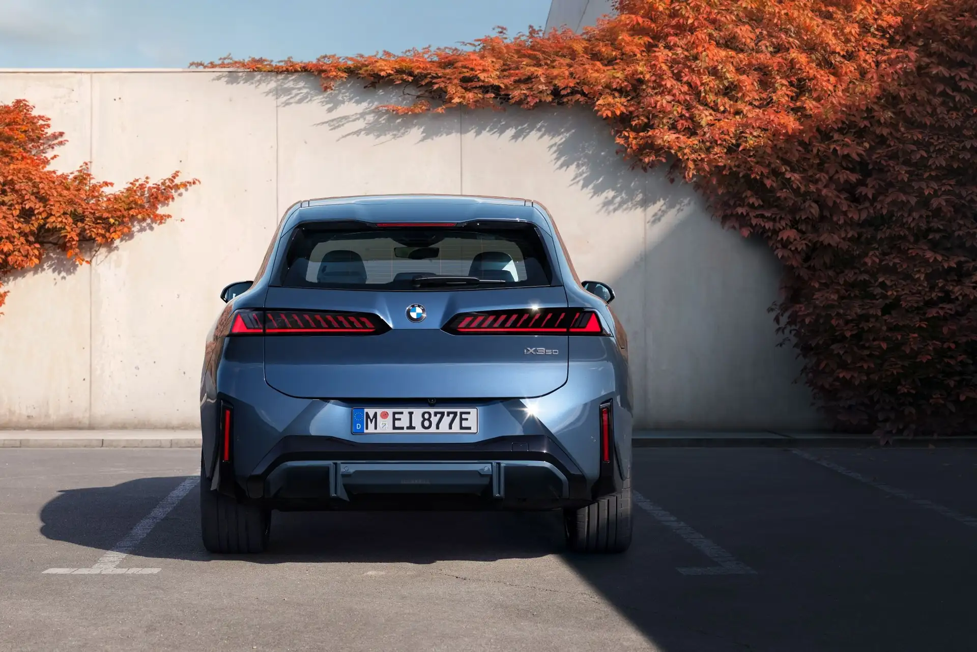 BMW IX3 von hinten in blau mit Mauer dahinter