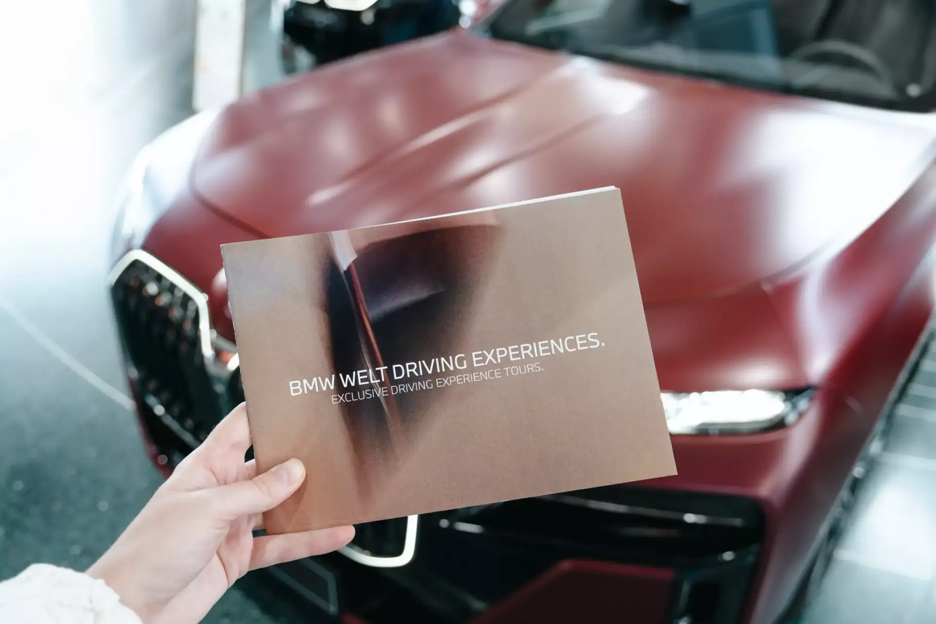 BMW und CarVia Roadbook wird in Hand gehalten vor BMW i7 roter Fronthaube