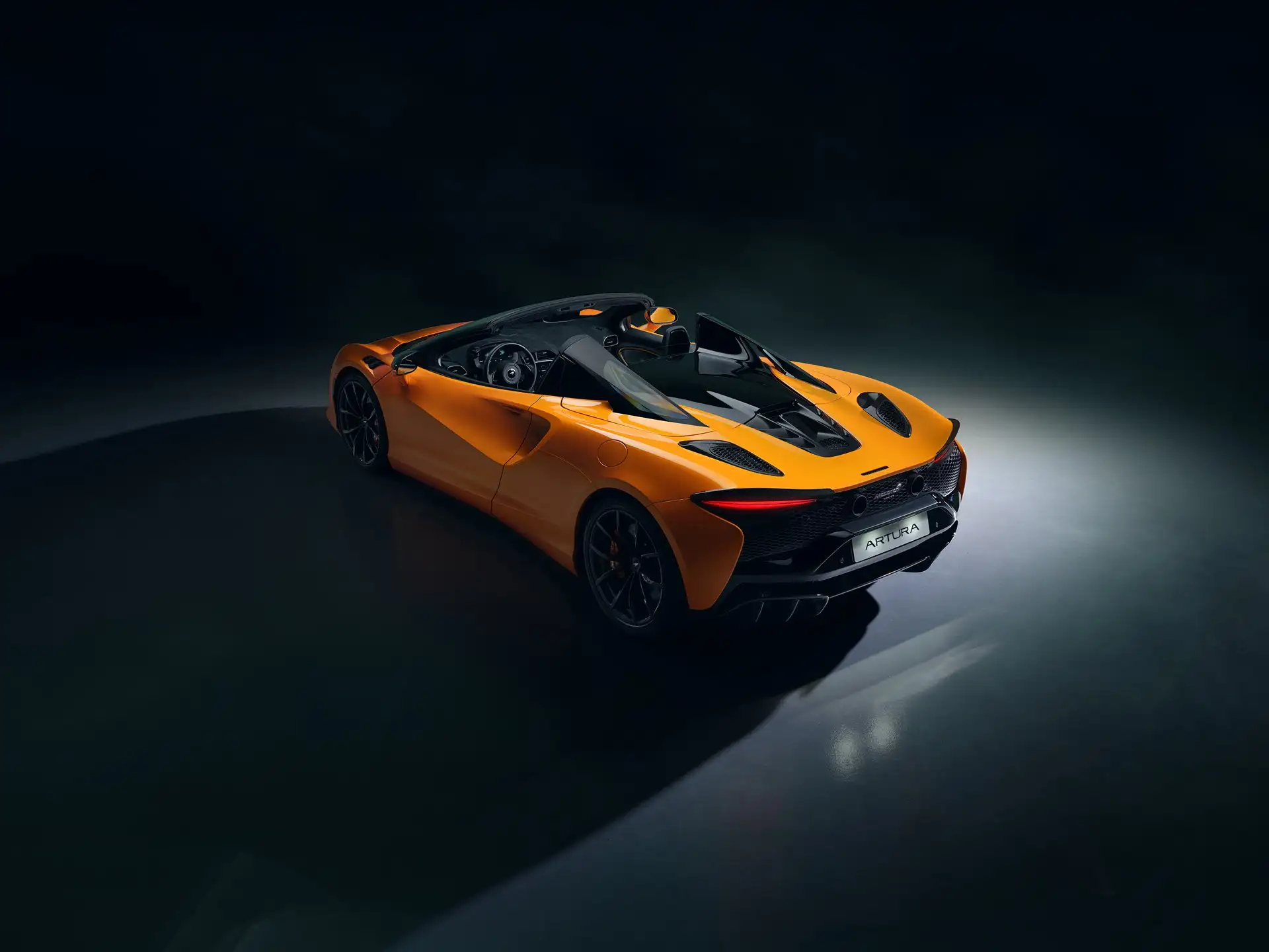 Mclaren Artura Spider in Orange Seite Heck Ansicht mit offenen Dach in dunkler Umgebung