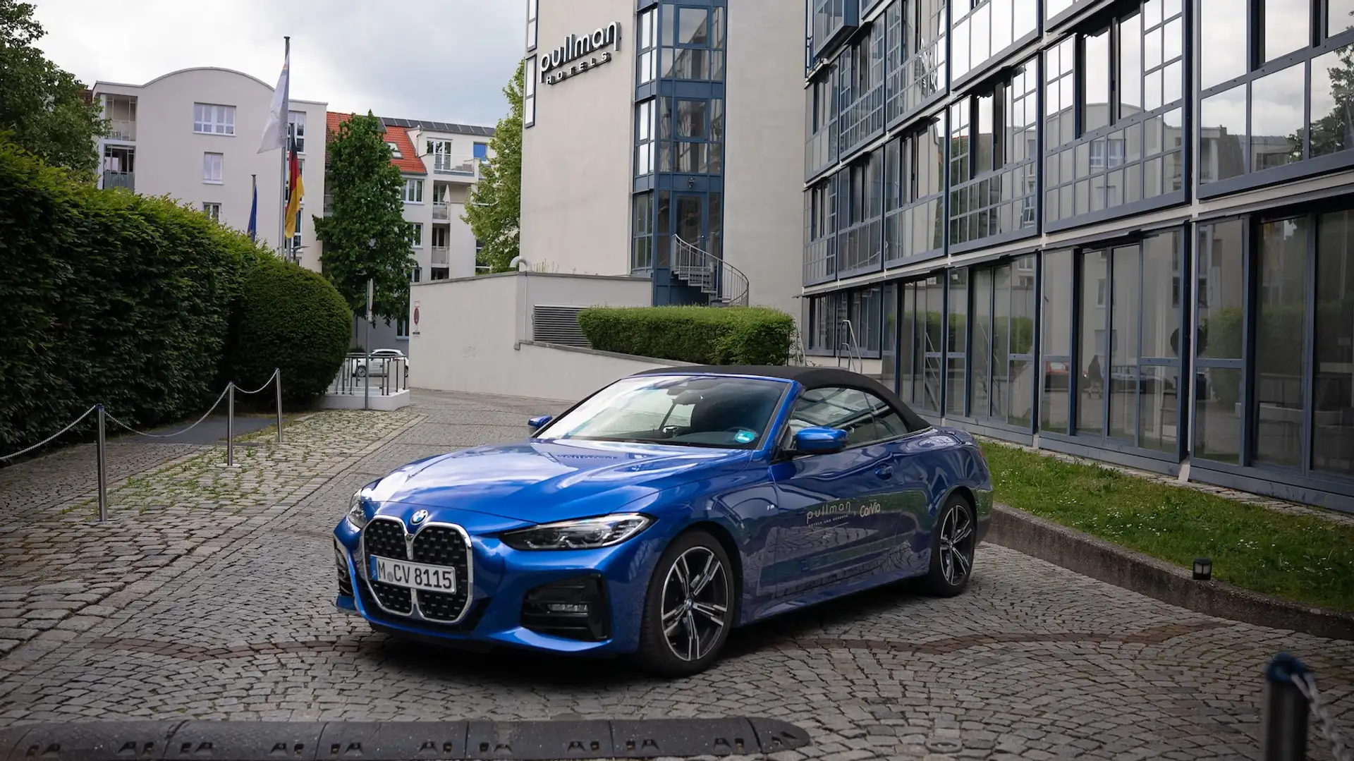 Blue BMW 4 Series convertible from the front in front of the hotel entrance with closed top